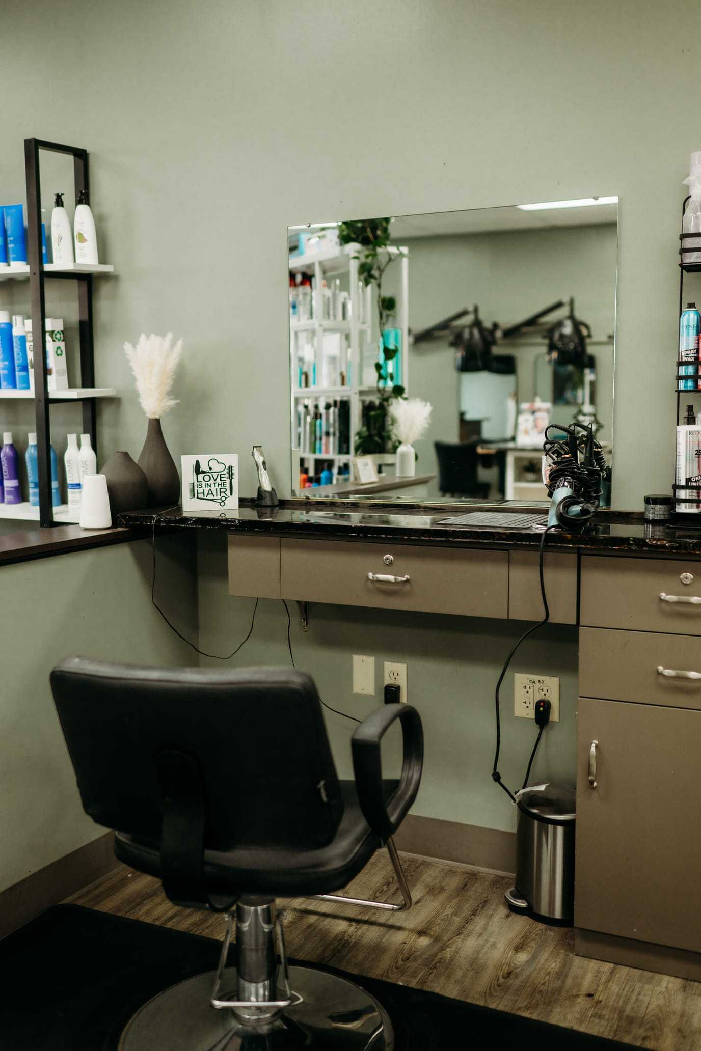 Hair salon station with styling chair, mirror, and hair products on shelves.